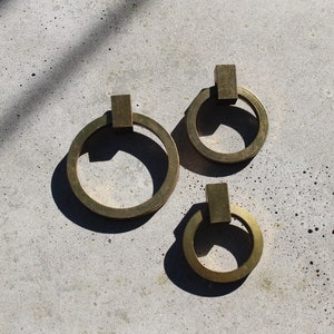 Peut inclure: Trois poignées de porte en laiton avec des poignées carrées. Les anneaux sont de tailles différentes.