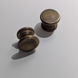Peut inclure: Deux boutons de cabinet en laiton avec un dessus rond et une base cannelée.