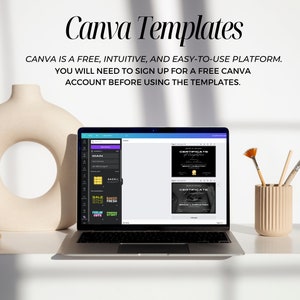May include: A laptop computer displaying Canva templates on the screen. The templates include a certificate design and a set of colorful labels. The laptop is on a white desk with a vase, paintbrushes, and a cup of paintbrushes.