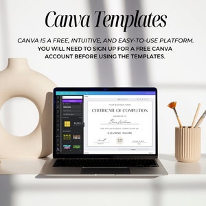 May include: A laptop computer displaying a Canva template for a certificate of completion. The template is white with black text and a gold seal. The laptop is on a white desk with a vase, rocks, and paintbrushes.