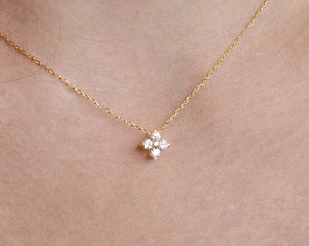 May include: A delicate gold necklace featuring a four-petal flower pendant with small, clear gemstones. The necklace is displayed on a person's neck, showcasing its fine chain and sparkling design. The jewelry is a subtle yet elegant accessory.