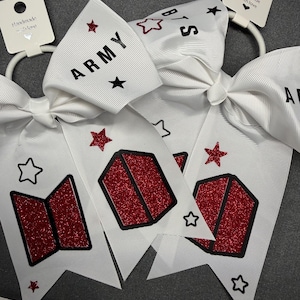 Può includere: Due fiocchi bianchi per capelli con il testo ARMY e BTS in caratteri neri. I fiocchi sono decorati con forme geometriche glitterate rosse e contorni di stelle neri. Ogni fiocco è fissato a un elastico bianco e a un'etichetta Handmade with love.