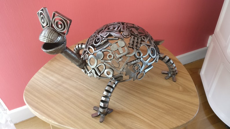 Peut inclure: Une sculpture de tortue en m&eacute;tal argent&eacute; r&eacute;alis&eacute;e &agrave; partir de pi&egrave;ces de m&eacute;tal recycl&eacute;es. La tortue a une carapace d&eacute;taill&eacute;e et un visage fantaisiste.