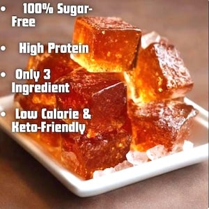 May include: A close-up of several amber-colored, square-shaped food items stacked on a white square plate. The image includes text that reads "100% Sugar-Free", "High Protein", "Only 3 Ingredient", and "Low Calorie & Keto-Friendly".