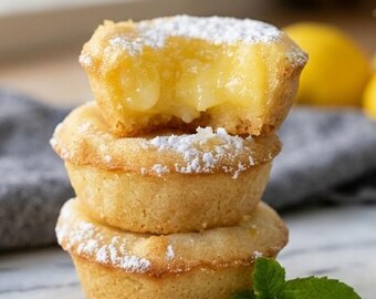 May include: A stack of three golden-brown mini lemon tarts with a shortbread crust, filled with a bright yellow lemon curd, and dusted with white powdered sugar. The top tart has a visible bite taken out of it, revealing the smooth filling.