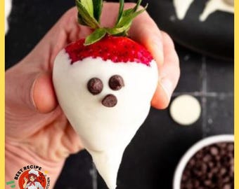 May include: A fresh strawberry dipped in white chocolate to resemble a ghost, featuring three small dark chocolate chips arranged as eyes and a mouth. The green leafy stem remains at the top, and the red fruit is visible beneath the white coating.
