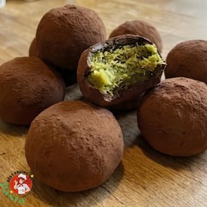 May include: A collection of chocolate truffles, dusted with cocoa powder. One truffle is cut open, revealing a green interior. The truffles are arranged on a wooden surface. The image is well-lit, showcasing the texture and color of the treats.
