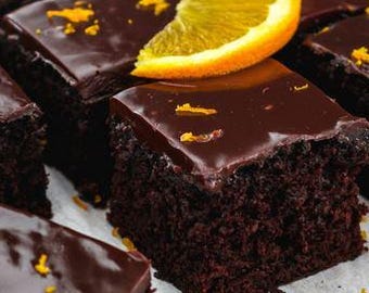 May include: Close-up of several square chocolate cakes with a glossy dark chocolate glaze. Each cake is topped with a slice of orange and orange zest. The cakes are arranged on a white surface.