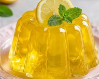 May include: A bright yellow lemon jelly dessert, garnished with a lemon slice and mint leaves, sits on a pink plate. The jelly has a fluted shape, and the dessert is presented in a close-up shot.