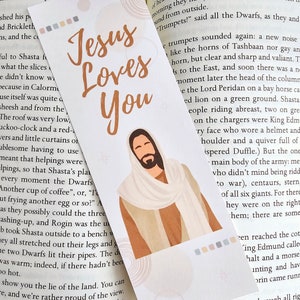 May include: A bookmark with a beige background and a brown illustration of Jesus with the text "Jesus Loves You".