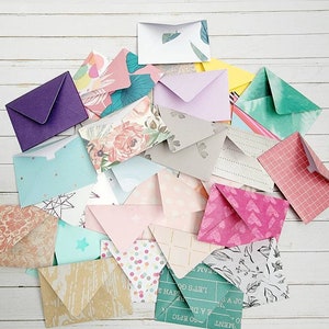 Peut inclure: Une collection d'enveloppes en papier coloré et à motifs de différentes tailles et designs. Les enveloppes présentent des motifs floraux, géométriques et abstraits dans des tons de rose, bleu, vert et violet. Elles sont disposées sur une surface en bois blanc.