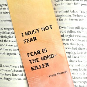 May include: A bookmark with a peach and orange gradient background. The bookmark features a black and white quote from Frank Herbert's Dune: "I must not fear. Fear is the mind-killer."