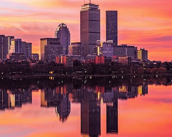 May include: A vibrant cityscape at sunset, with tall buildings silhouetted against a sky of orange, pink, and purple hues. The buildings' reflections mirror in the calm water below, creating a symmetrical and colorful scene.
