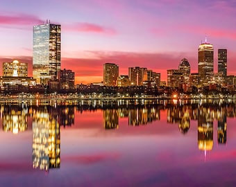 May include: A panoramic view of a city skyline at sunset, with tall buildings reflected in the water. The sky is a vibrant pink and purple, and the buildings are lit up with warm yellow lights.