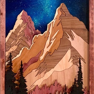 Puede incluir: Una talla de madera de una cordillera con un cielo nocturno estrellado arriba. Las monta&ntilde;as est&aacute;n hechas de diferentes tipos de madera, creando un efecto de capas. Una silueta de una persona se encuentra en primer plano, rodeada de &aacute;rboles.