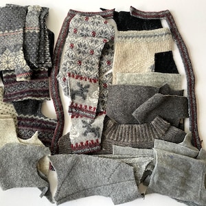 May include: A collection of grey and off-white knitted fabric pieces, some with red and white patterned designs. The pieces include sections of sweaters and other garments, with visible seams and textures. The arrangement is on a white background.