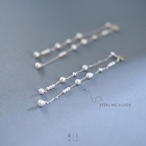 Pu&ograve; includere: Eleganti orecchini pendenti in argento sterling con un delicato design a catena ornato da piccole perle lucenti. Gli orecchini hanno una forma allungata e aggraziata, perfetta per aggiungere un tocco di raffinatezza. Il testo "STERLING SILVER" &egrave; visibile.