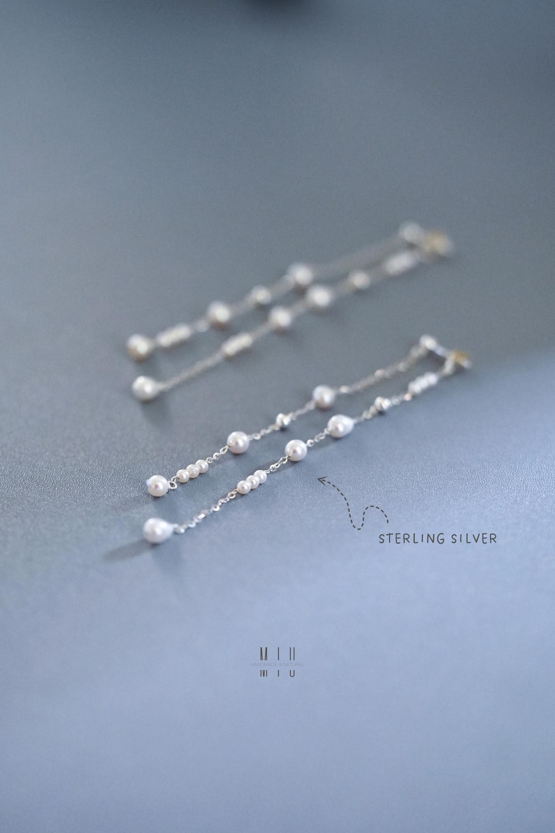 Pu&ograve; includere: Eleganti orecchini pendenti in argento sterling con un delicato design a catena ornato da piccole perle lucenti. Gli orecchini hanno una forma allungata e aggraziata, perfetta per aggiungere un tocco di raffinatezza. Il testo "STERLING SILVER" &egrave; visibile.