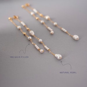 Pu&ograve; includere: Eleganti orecchini in oro riempito con perle naturali. Gli orecchini presentano un delicato design a catena con pi&ugrave; piccole perle e una perla pi&ugrave; grande a forma di goccia. Il testo "14K GOLD FILLED" e "NATURAL PEARL" sono visibili.