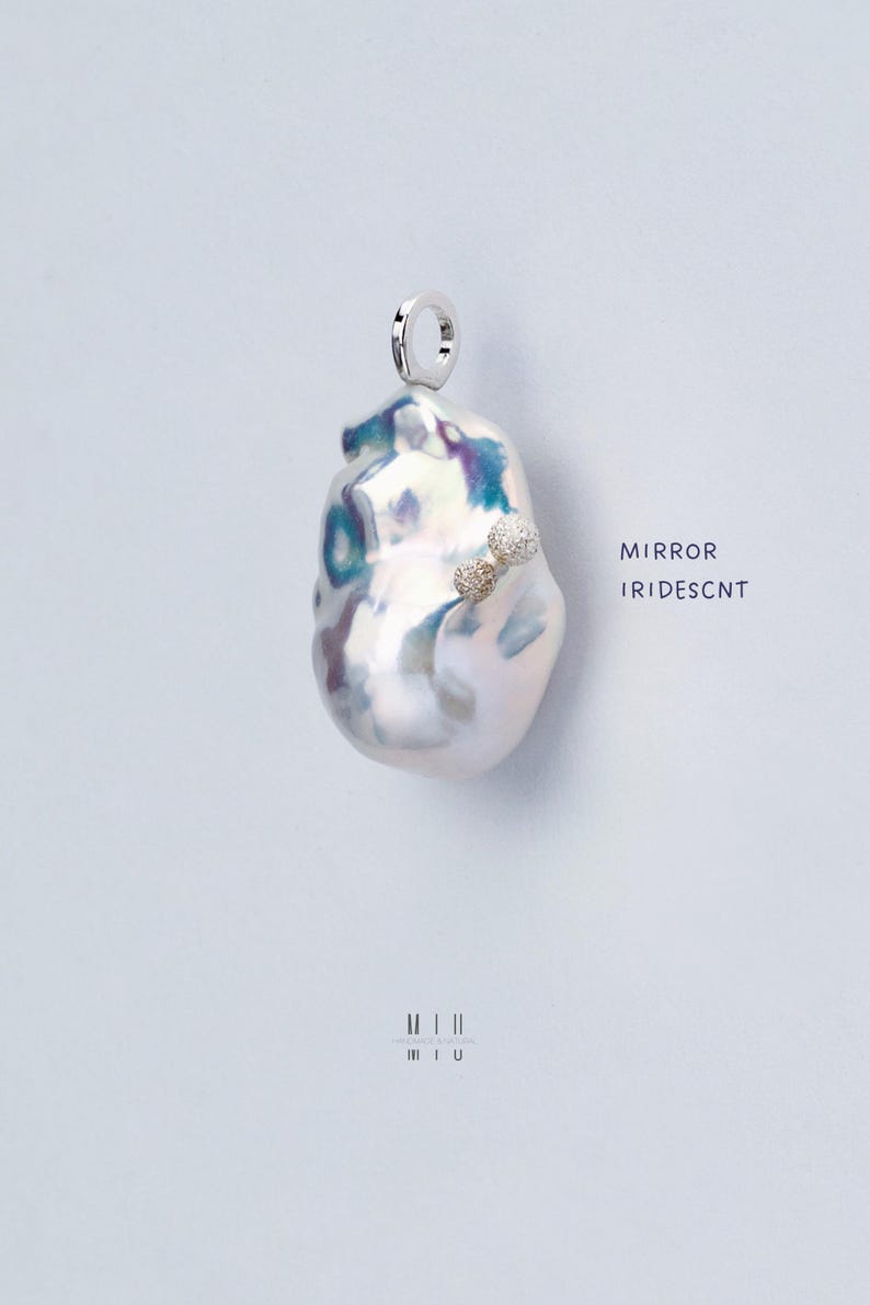 May include: A white baroque pearl pendant with a silver loop and two small diamond accents. The pearl has an iridescent sheen and the text "MIRROR IRIDESCNT" is written below it.
