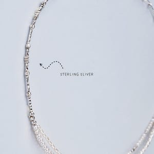 K&ouml;nnte beinhalten: Eine zarte Halskette aus Sterlingsilber mit mehreren Str&auml;ngen. Die Halskette hat kleine, runde Perlen und strukturierte Silberelemente. Der Text "STERLING SILVER" ist im Bild sichtbar. Die Halskette wird vor einem hellen Hintergrund pr&auml;sentiert.