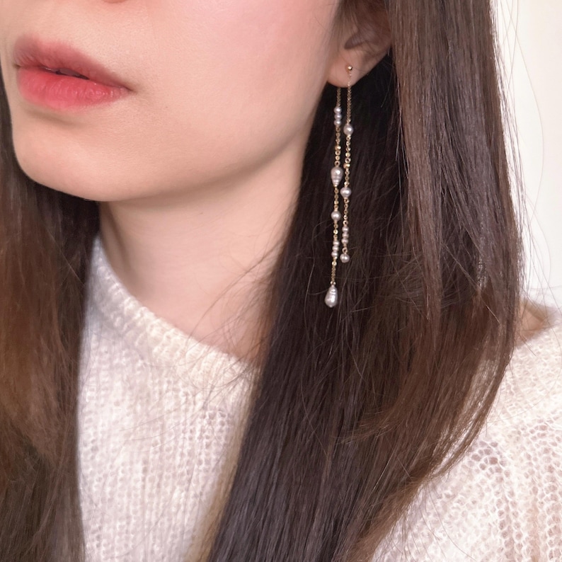 Pu&ograve; includere: Orecchini pendenti color oro con pi&ugrave; fili di piccole perle e una perla pi&ugrave; grande a forma di goccia alla fine di ogni filo. Gli orecchini sono delicati ed eleganti, con un design semplice.