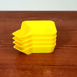May include: Three bright yellow plastic trays stacked on top of each other. The trays are rectangular with rounded corners and a slight lip around the edge.