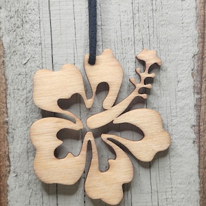 May include: A wooden hibiscus flower pendant with a black cord. The pendant is cut from light-colored wood, showcasing the flower's intricate details. The flower has five petals and a central stem.