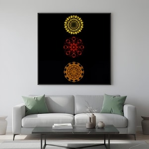 Peut inclure: Une œuvre d'art encadrée présentant trois motifs circulaires symétriques en jaune, rouge et orange sur fond noir. L'œuvre est accrochée au-dessus d'un canapé gris avec des coussins verts, créant une ambiance de salon moderne.