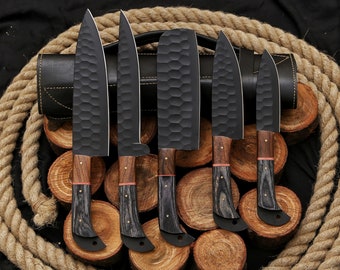 May include: A set of six black kitchen knives with wooden handles. The knives are arranged in a row on a wooden surface. The knives have a textured, hammered finish.
