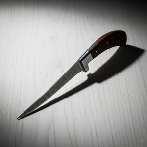 May include: A long, slender knife with a dark wood handle and a textured, silver blade. The handle is curved and secured with small rivets. The knife is angled, casting a shadow on the light-colored surface.