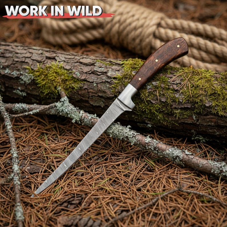 May include: A hunting knife with a patterned steel blade and a dark wood handle. The handle is secured with brass rivets. The knife rests on a bed of pine needles and a moss-covered log. The text "WORK IN WILD" is in the upper left corner.