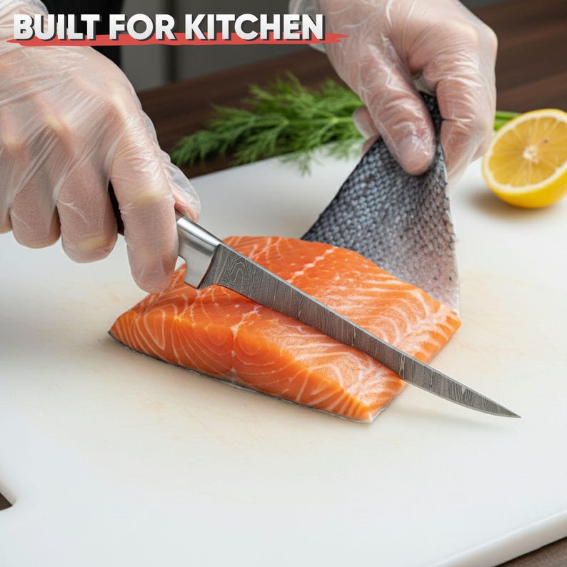 May include: A fillet knife slicing through a salmon fillet on a white cutting board. The salmon is bright orange, and the knife has a patterned blade. The text "BUILT FOR KITCHEN" is at the top.