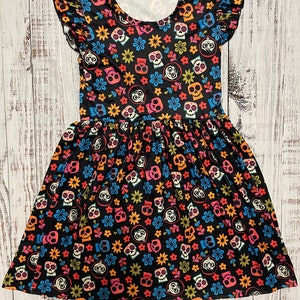 May include: A black dress with a colorful print of sugar skulls and flowers. The dress has short sleeves with ruffles and a gathered skirt.