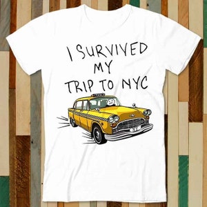 May include: White t-shirt with the text "I survived my trip to NYC" in black marker. A yellow taxi cab with a cartoon driver is pictured below the text.