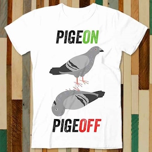 Könnte beinhalten: Weißes T-Shirt mit einer schwarzen und grünen Grafik eines Taubens mit dem Text "PIGEON" darüber und einer schwarzen und roten Grafik eines Taubens mit dem Text "PIGE OFF" darunter.