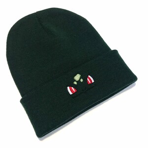 May include: Dark green beanie hat with a turned-up hem. The hat has an embroidered cartoon character face in green, red, and white. The beanie is made of a soft, knitted fabric.