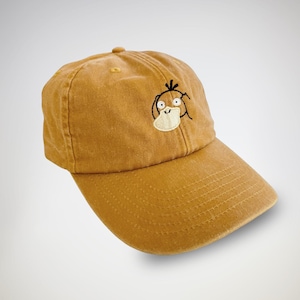 May include: Mustard-coloured baseball cap with an embroidered cartoon character. The cap has a curved peak and an adjustable strap. This playful accessory is a great addition to any outfit.