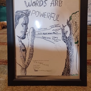 May include: A black and white drawing of two trees with words written on them. The words are "You're ugly", "You're leaves are thorny", "Why are you here", "You'll never make fruit", "Stupid tree", "I shall just cut you down". The drawing is framed in a black frame. The text at the bottom of the drawing reads "Death and Life are in the power of the tongue", "Your words are powerful, even with trees", "Proverbs 18:21", "Trees...so watch your words!!".