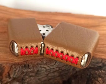 May include: A brown leather lighter case with red stitching. The case is closed and the stitching is visible on both sides.
