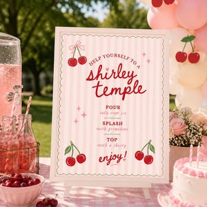 May include: A sign on a white easel with the text "Help Yourself to a Shirley Temple." The sign has a pink and white striped background with cherry illustrations. Other elements include a pink drink dispenser, bottles, and a cake.