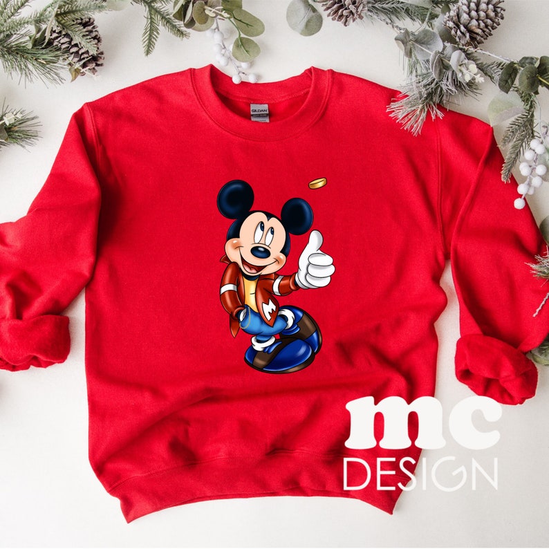 K&ouml;nnte beinhalten: Roter Pullover mit einem Cartoon-Bild von Mickey Mouse, der eine rote Jacke und eine blaue Jeans tr&auml;gt und den Daumen nach oben streckt. Der Text "mc DESIGN" ist auf der Unterseite des Pullovers aufgedruckt.