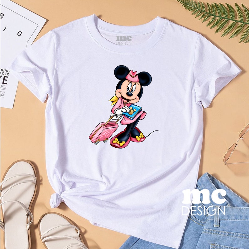 May include: White t-shirt with a cartoon image of Minnie Mouse dressed as a flight attendant, pulling a pink suitcase. The text "mc DESIGN" is printed on the shirt.