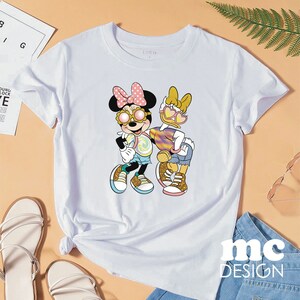 Op de afbeelding: Wit T-shirt met een grafische print van Minnie Mouse en Daisy Duck die een zonnebril dragen en een lolly vasthouden. De tekst "SHEIN" staat op het T-shirt gedrukt.