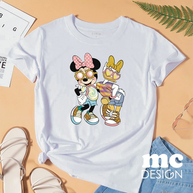 Op de afbeelding: Wit T-shirt met een grafische print van Minnie Mouse en Daisy Duck die een zonnebril dragen en een lolly vasthouden. De tekst "SHEIN" staat op het T-shirt gedrukt.
