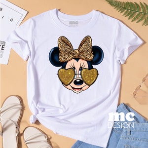 May include: White t-shirt featuring a cartoon mouse wearing heart-shaped sunglasses with gold glitter. The mouse has a black bow with a leopard print. The text "mc DESIGN" is on the shirt.