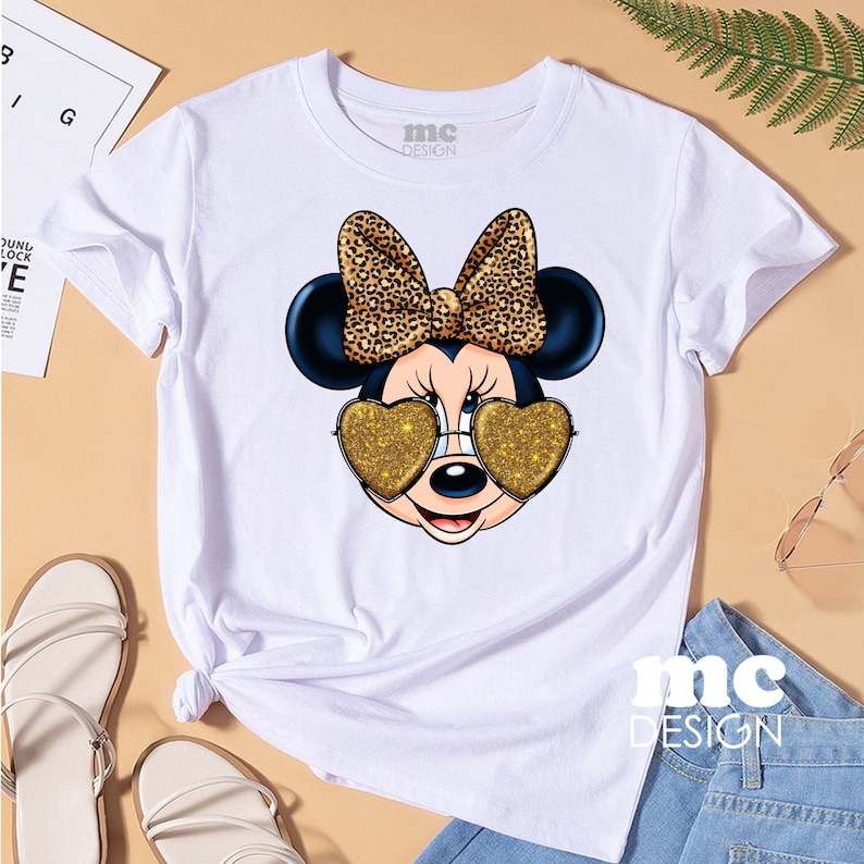 May include: White t-shirt featuring a cartoon mouse wearing heart-shaped sunglasses with gold glitter. The mouse has a black bow with a leopard print. The text "mc DESIGN" is on the shirt.
