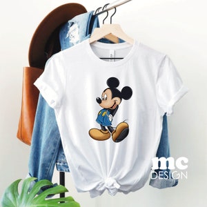 May include: White t-shirt with a cartoon image of Mickey Mouse in his signature red shorts and yellow shoes. The shirt has a crew neck and short sleeves.
