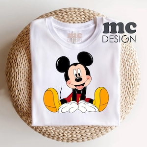 May include: White t-shirt with a cartoon image of Mickey Mouse sitting down. The shirt has the text "mc DESIGN" printed on the right side.