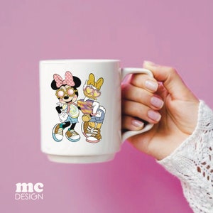 Op de afbeelding: Een witte keramische mok met een kleurrijke illustratie van twee cartoonfiguren die een zonnebril dragen. De personages zijn een muis met roze oren en een eend met gele veren. De mok heeft een zwart handvat.